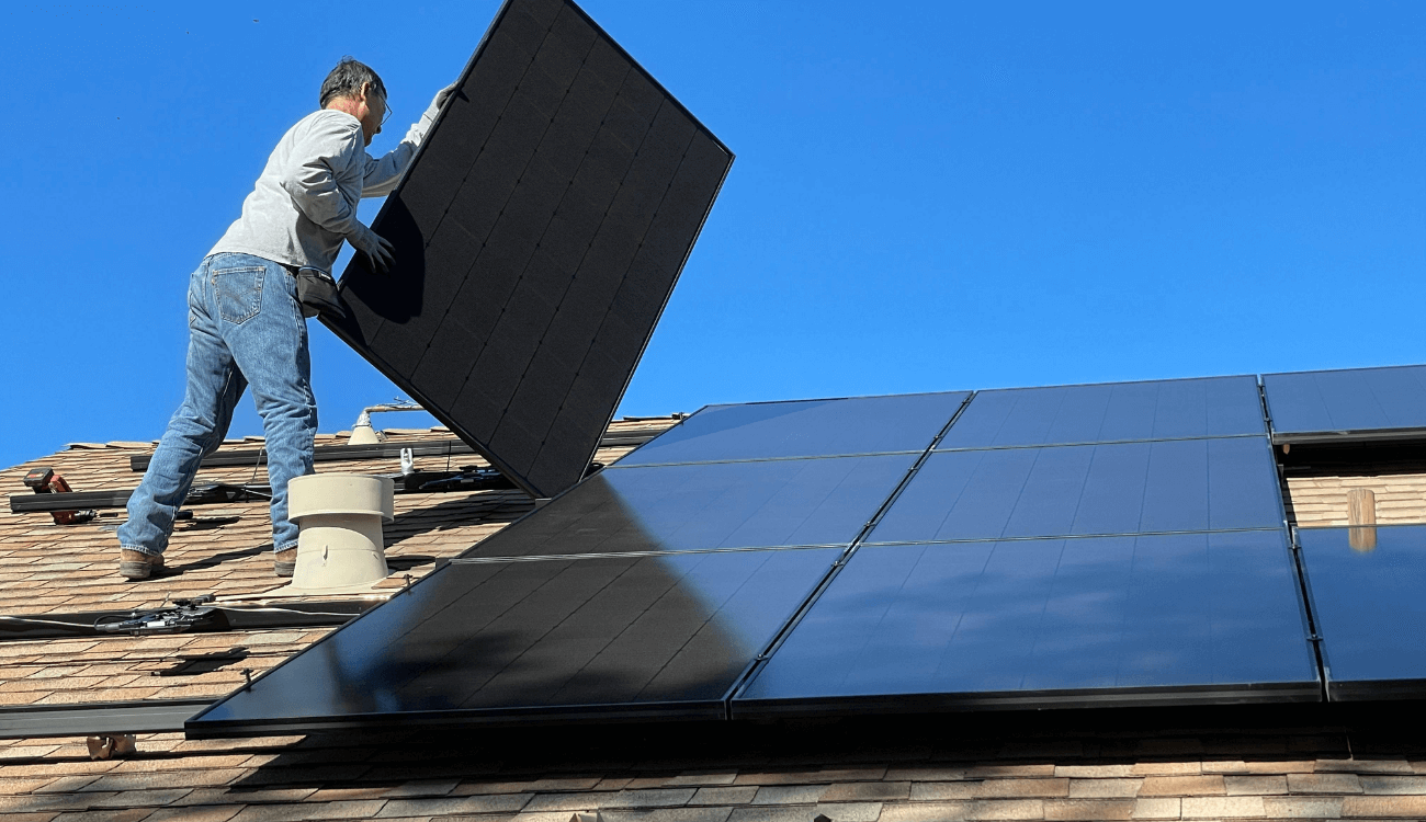A man installing black solar panels on a roof
